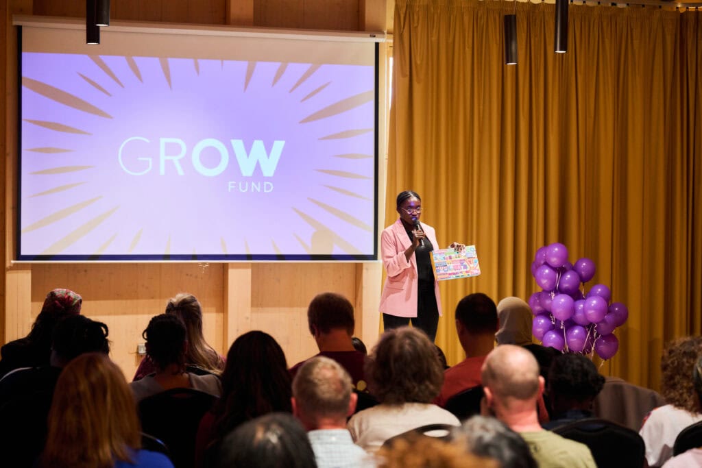 Christina speaking on stage with a microphone with a GROW poster in the background,.