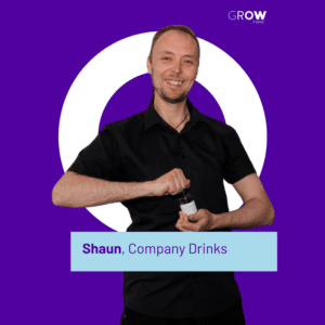 Shaun, Founder of Company Drinks is holding a drink while stood smiling infront of a purple background