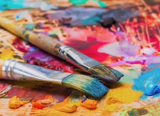 Used brushes on an artist’s palette of colorful oil paint